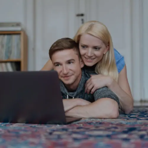 A young couple sitting on a patterned rug looking at a laptop